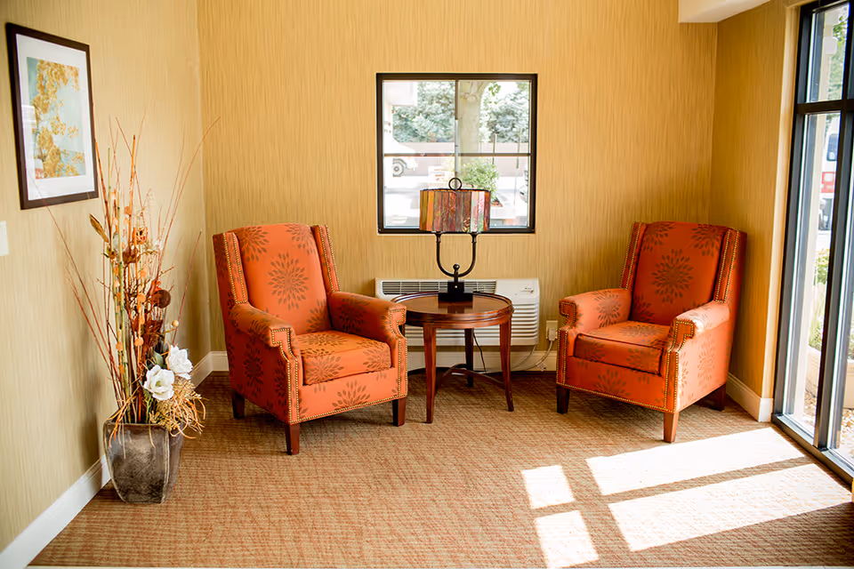 Two orange patterned chairs flank a round table with a lamp in a cozy lounge.