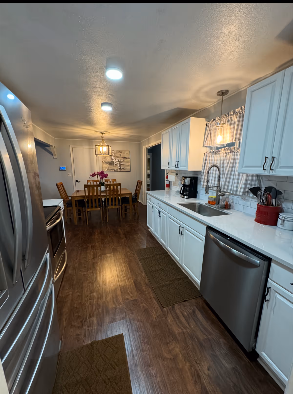 Bright kitchen with white cabinets, stainless appliances, sink, and dining table in back.