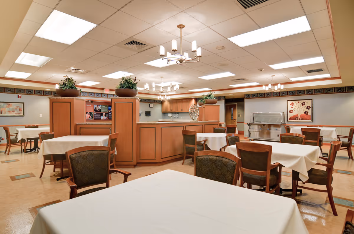 Interior view of a senior living dining room with tables, chairs, and a central counter.