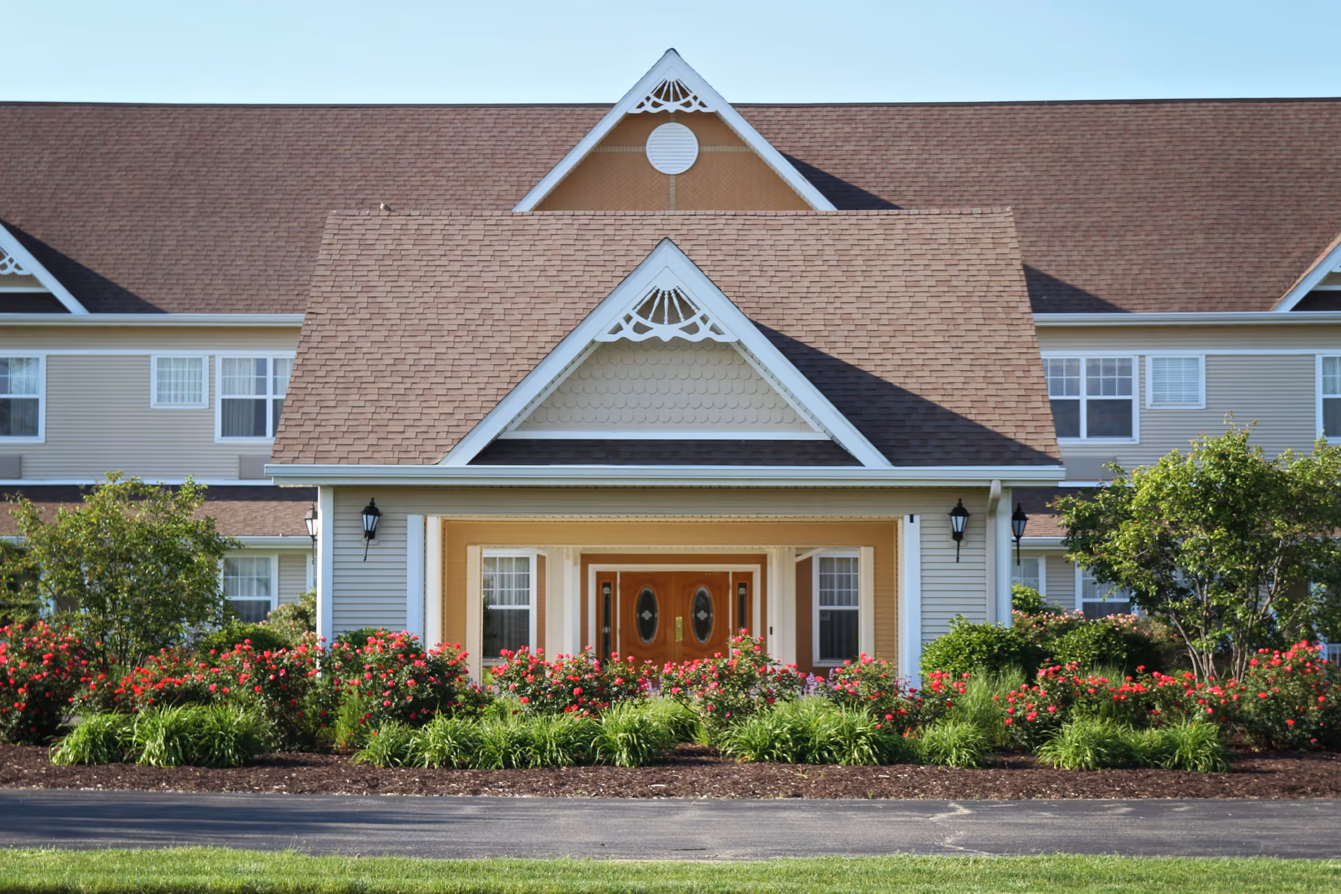 Senior living facility exterior with a welcoming front entrance and neatly landscaped flower beds.