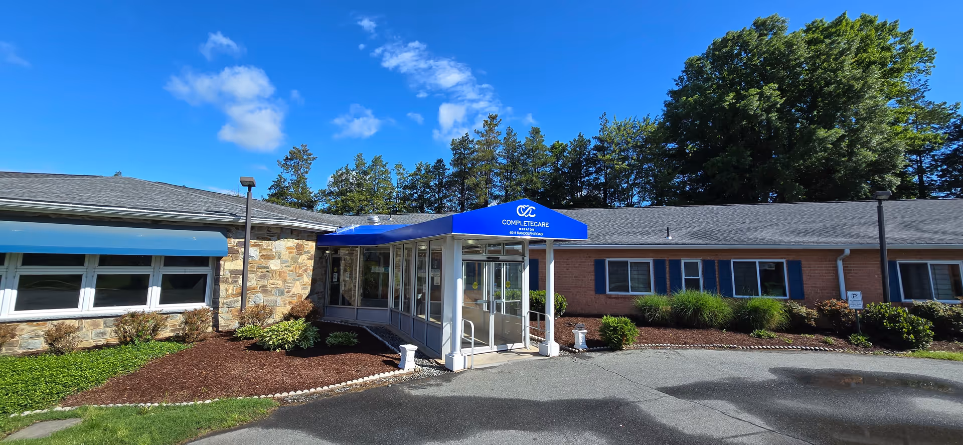 Exterior view of Complete Care at Wheaton entrance with blue canopy and brick building.