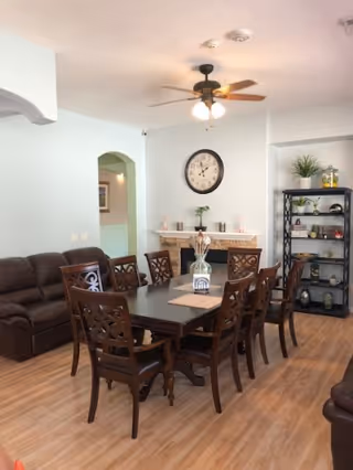 A dining area with a long table, eight chairs, and a brown leather sofa nearby.