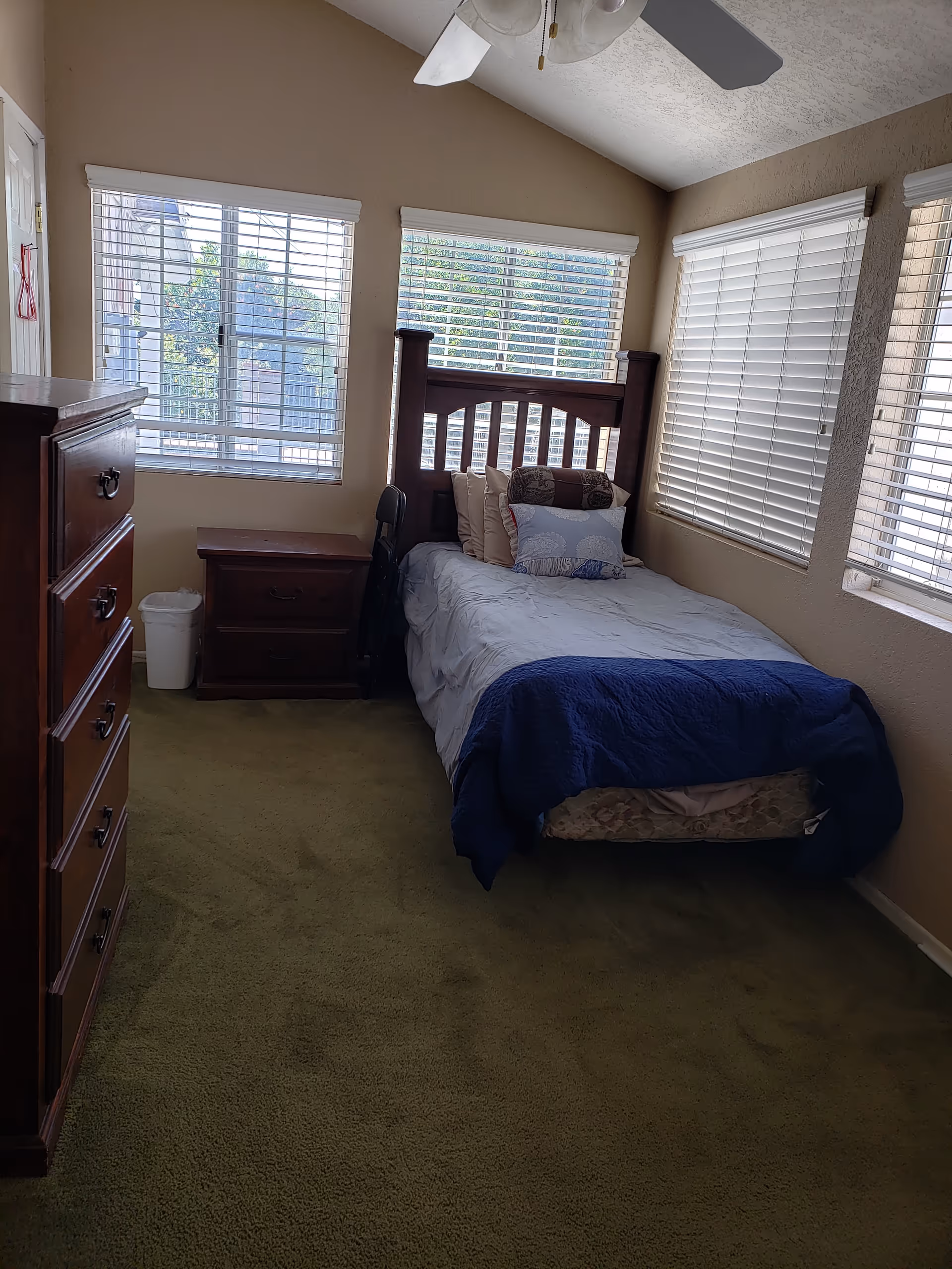 A single bedroom with a wooden bed, dresser, and ceiling fan.