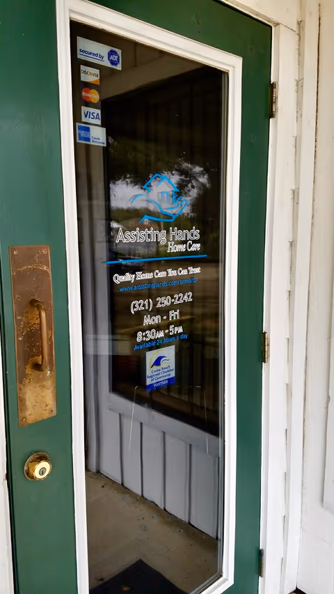 Green exterior door with glass panel displaying Assisting Hands Home Care logo and contact details.