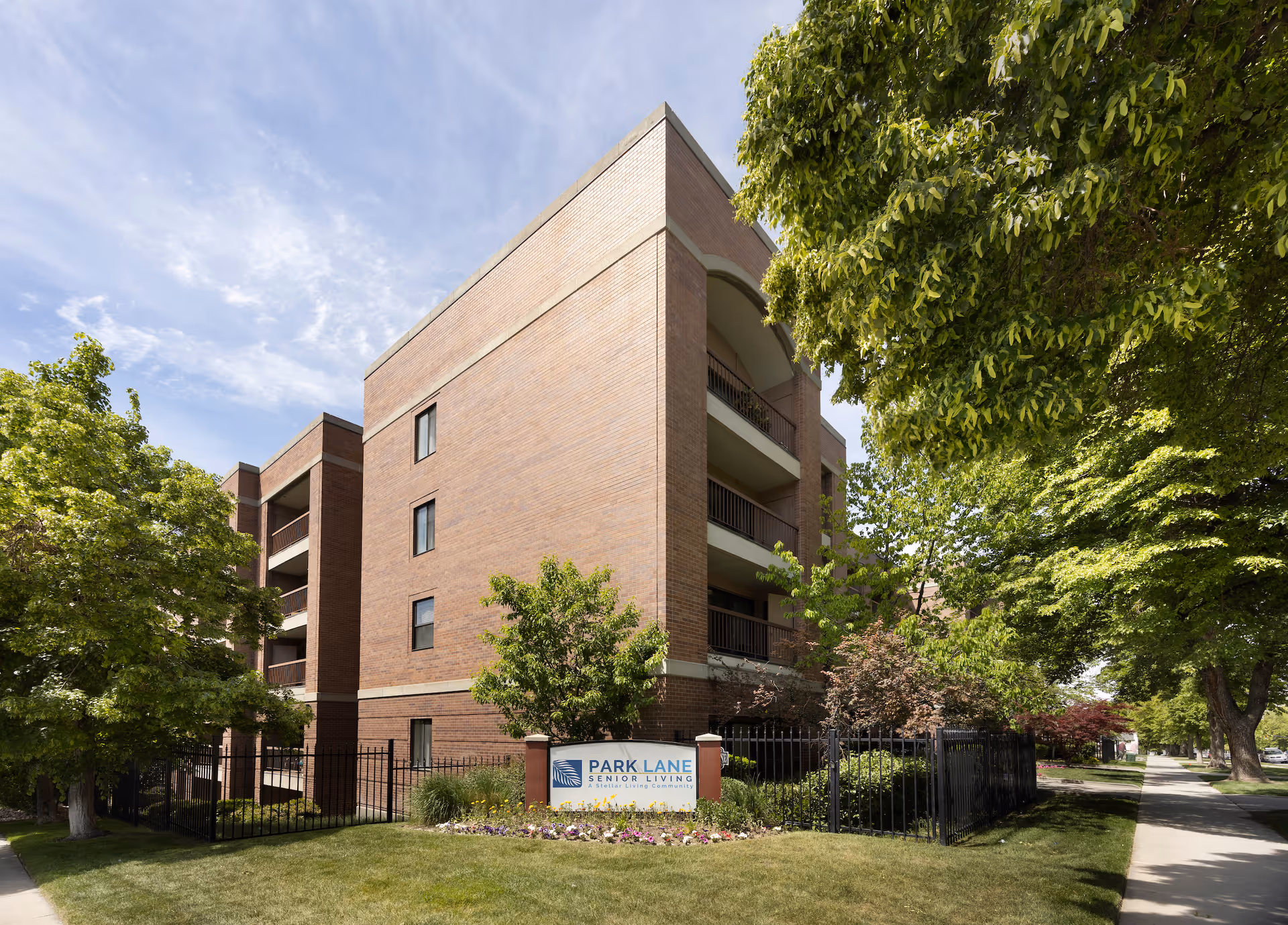 Brick four-story Park Lane Senior Living building with balconies, trees, and a sidewalk