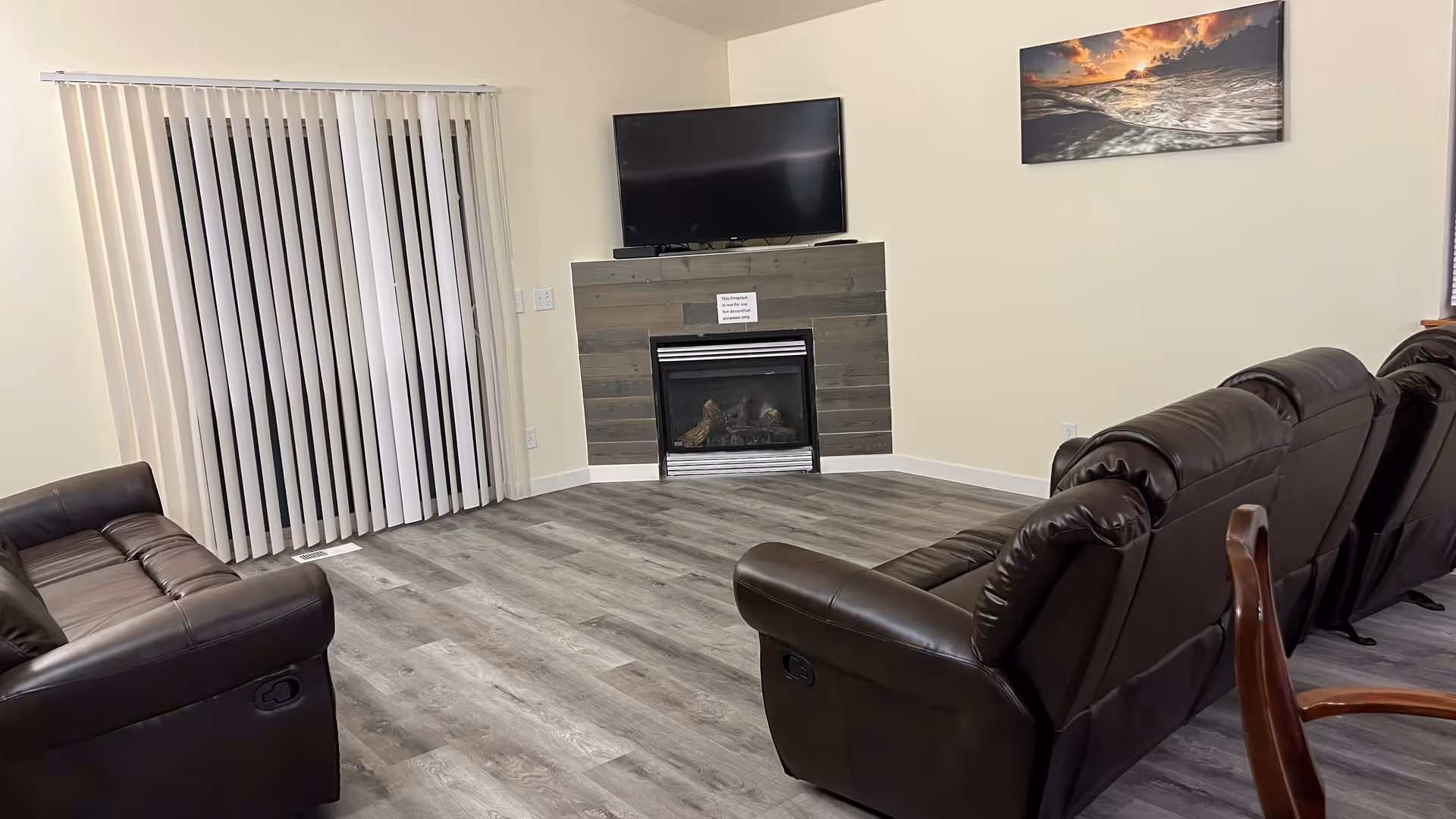Communal living room with leather recliners, a fireplace, TV, and vertical blinds along a sliding door.