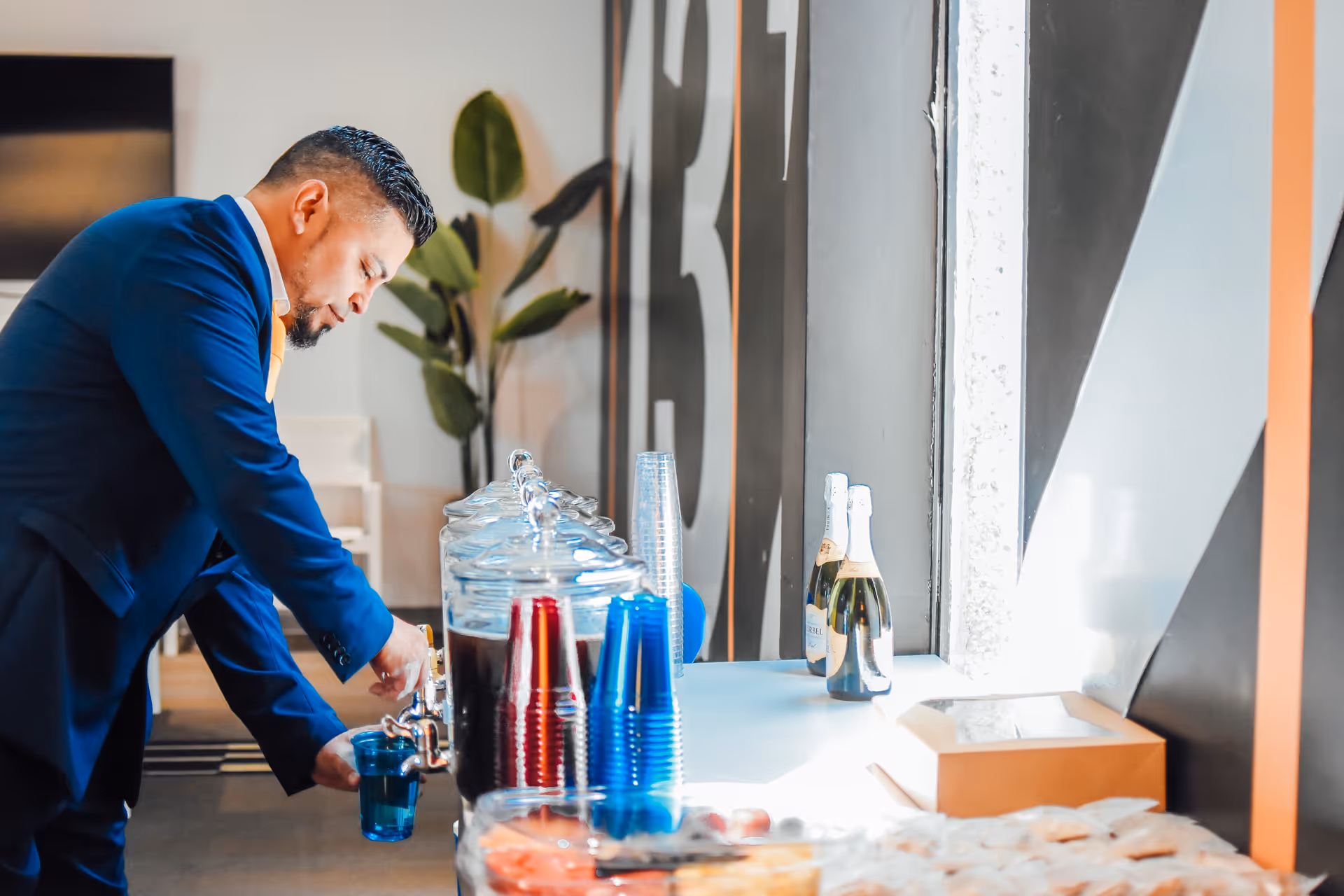 Staff member in blue suit prepares drinks at a beverage station indoors.