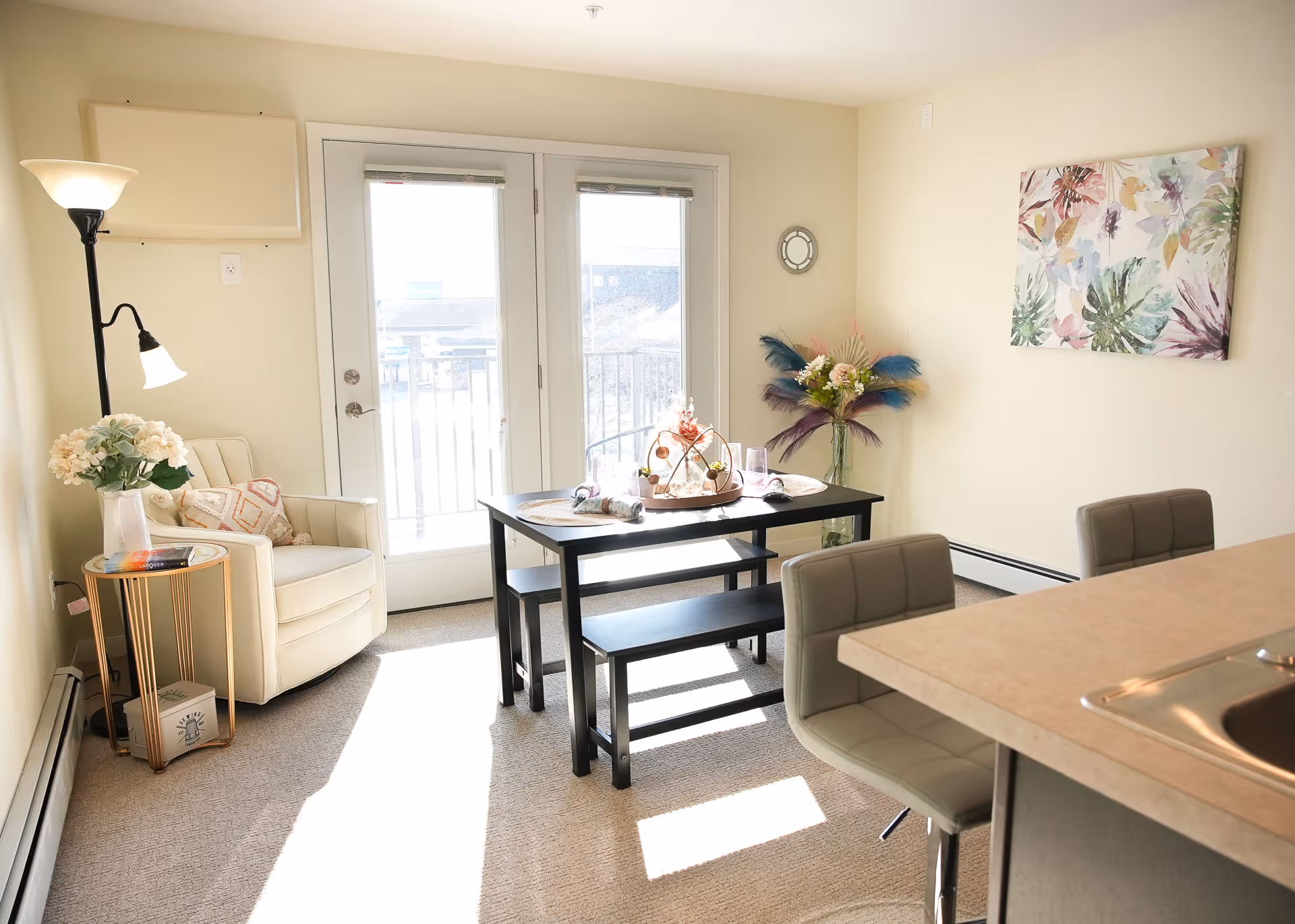 Bright interior dining area with a table, benches, chairs, plants, and balcony doors.