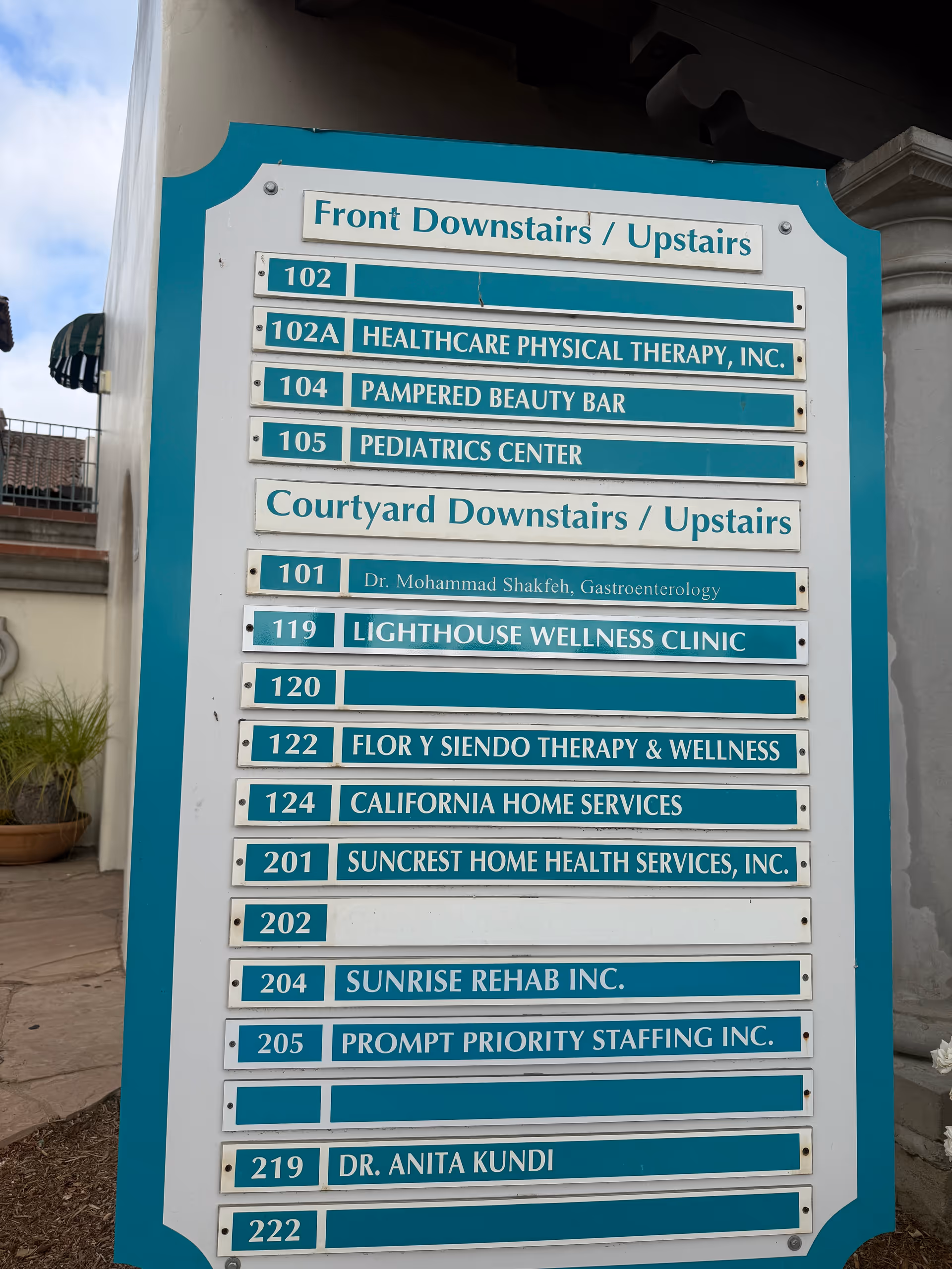 Teal-framed building directory sign listing suite numbers and names outside Sunrise Rehab Inc.