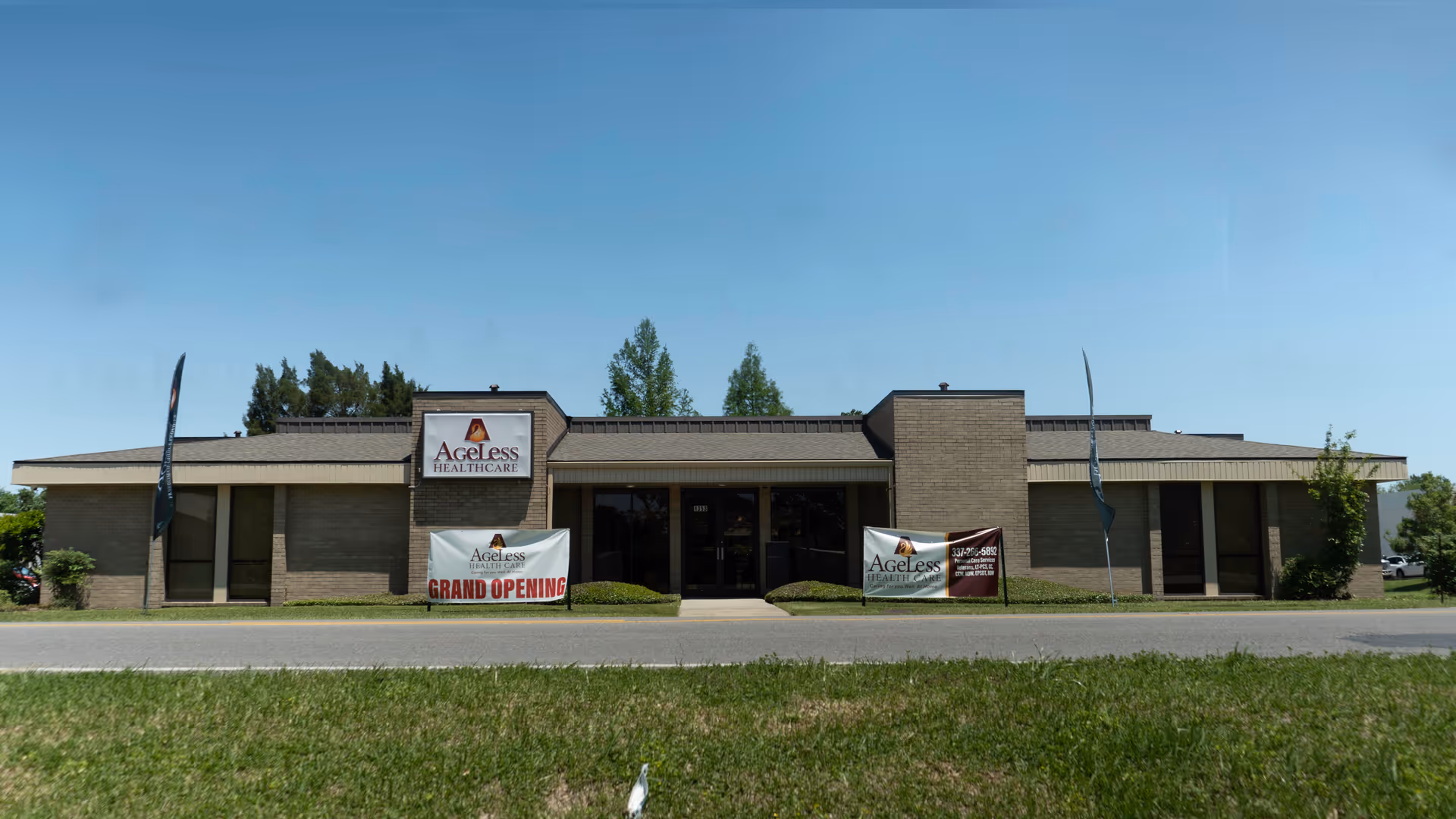 Front view of a single-story Ageless Healthcare building with banners and blue sky.