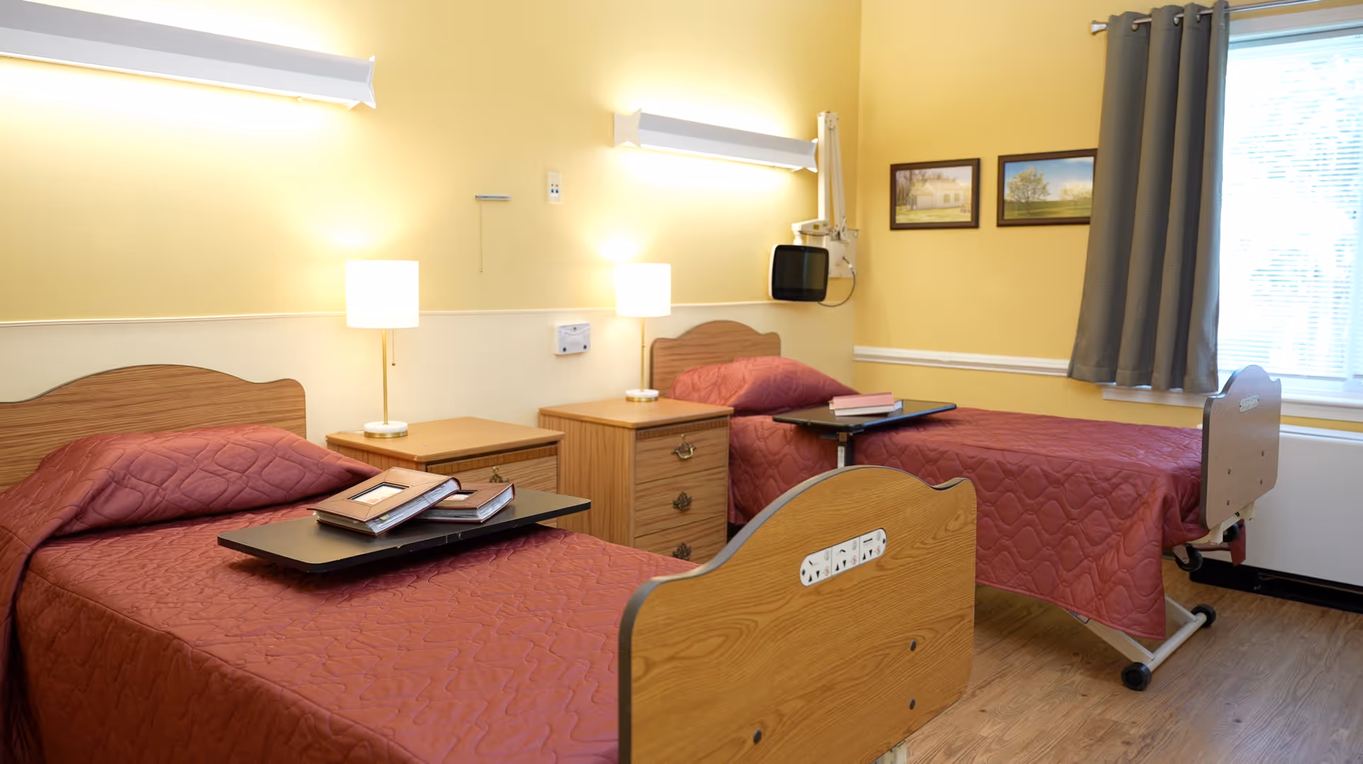 Two single beds with red quilts in a bright, shared senior living bedroom.