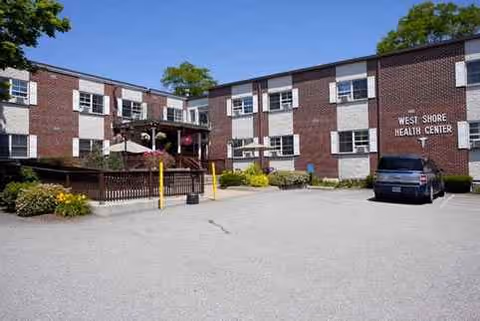 West Shore Health Center exterior brick building with parking lot and small seating area.