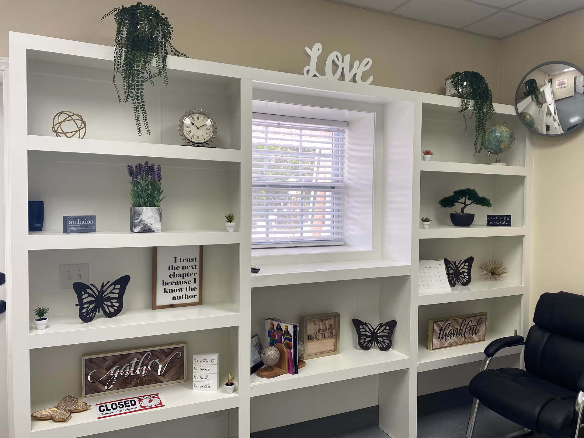 Interior of a senior living space with white shelves, plants, and decorative items around a window.