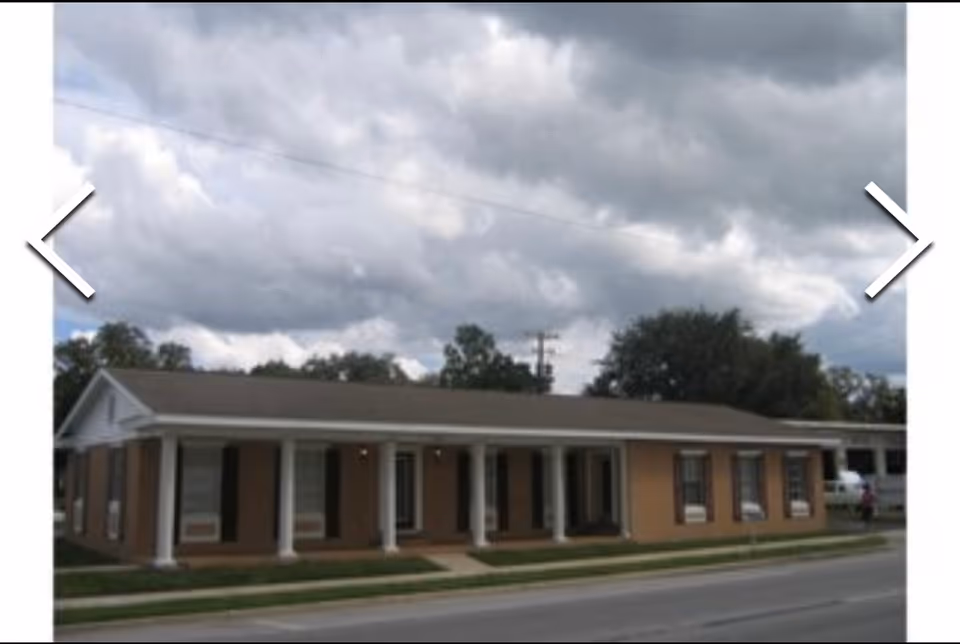 Single-story brick building with a covered front porch and white columns along a street.