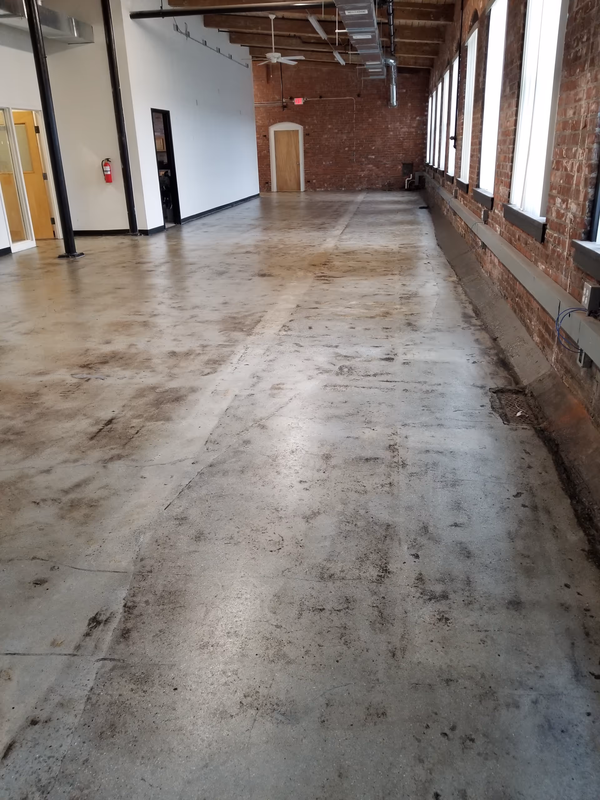 Long empty industrial hallway inside a building with brick walls and large windows.