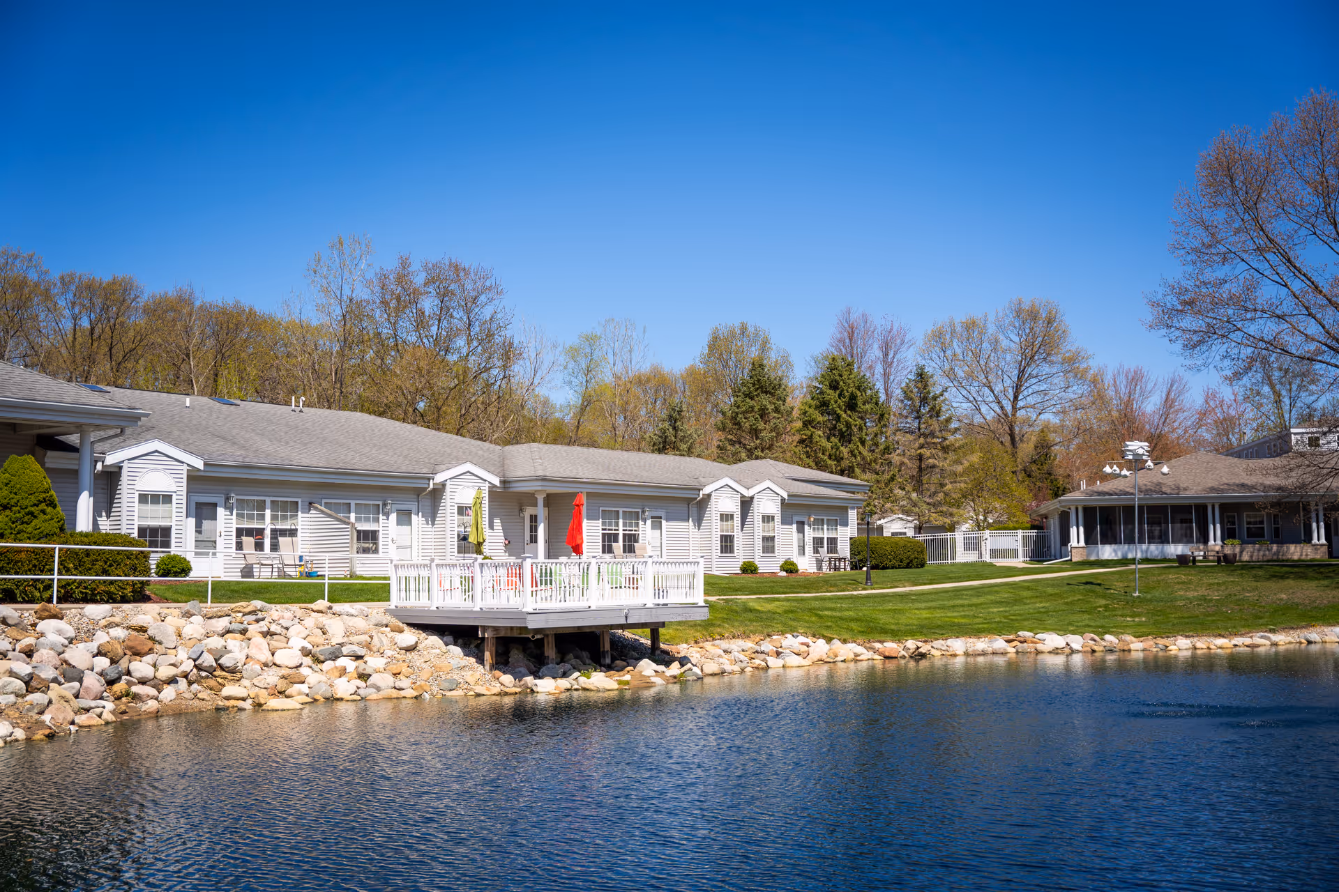 Woodland Terrace exterior residence rows along a lake with deck, lawn, and blue sky.