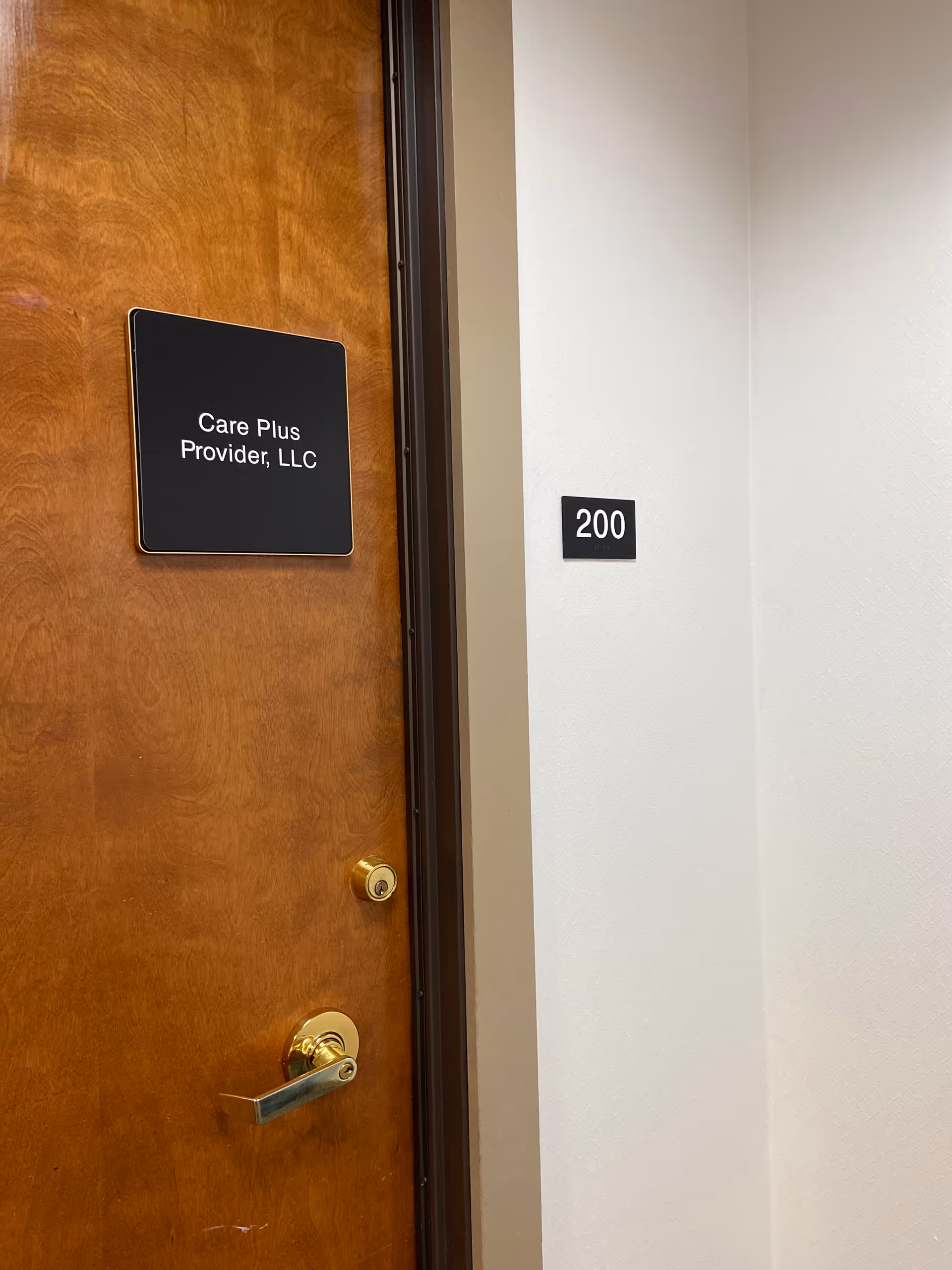 Wooden door with Care Plus Provider, LLC sign and room number 200 on white wall