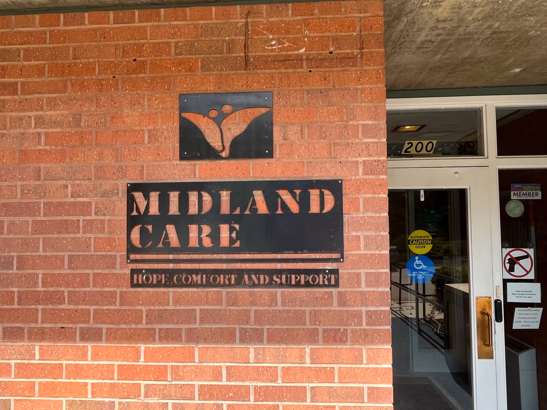 Brick building exterior with Midland Care sign and entrance door labeled 200.