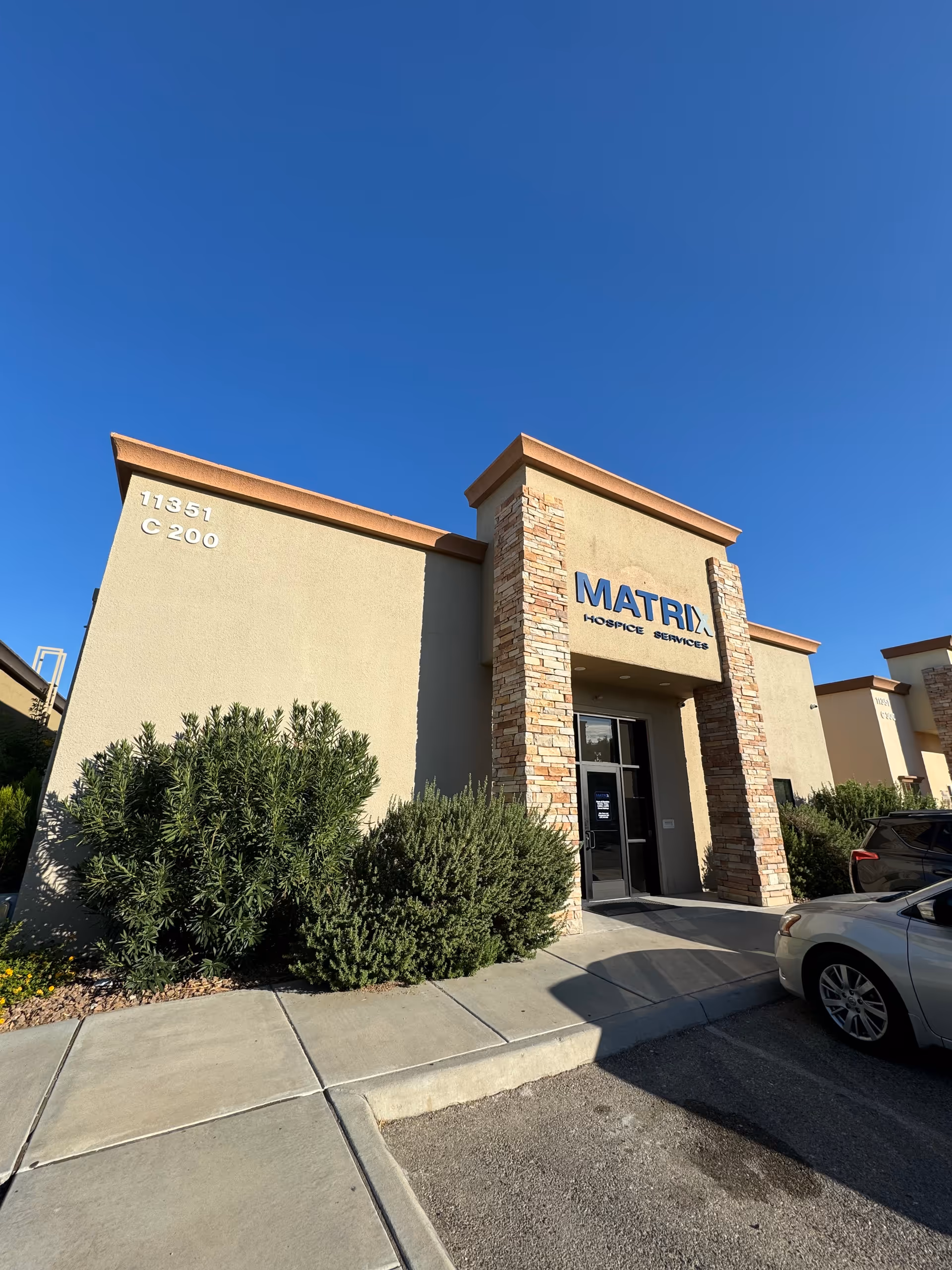 Exterior view of Matrix Hospice Services building entrance with stone columns and blue sky.