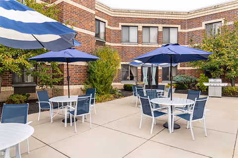 Outdoor patio at Elderwood at Cheektowaga featuring blue umbrellas and white tables with chairs.