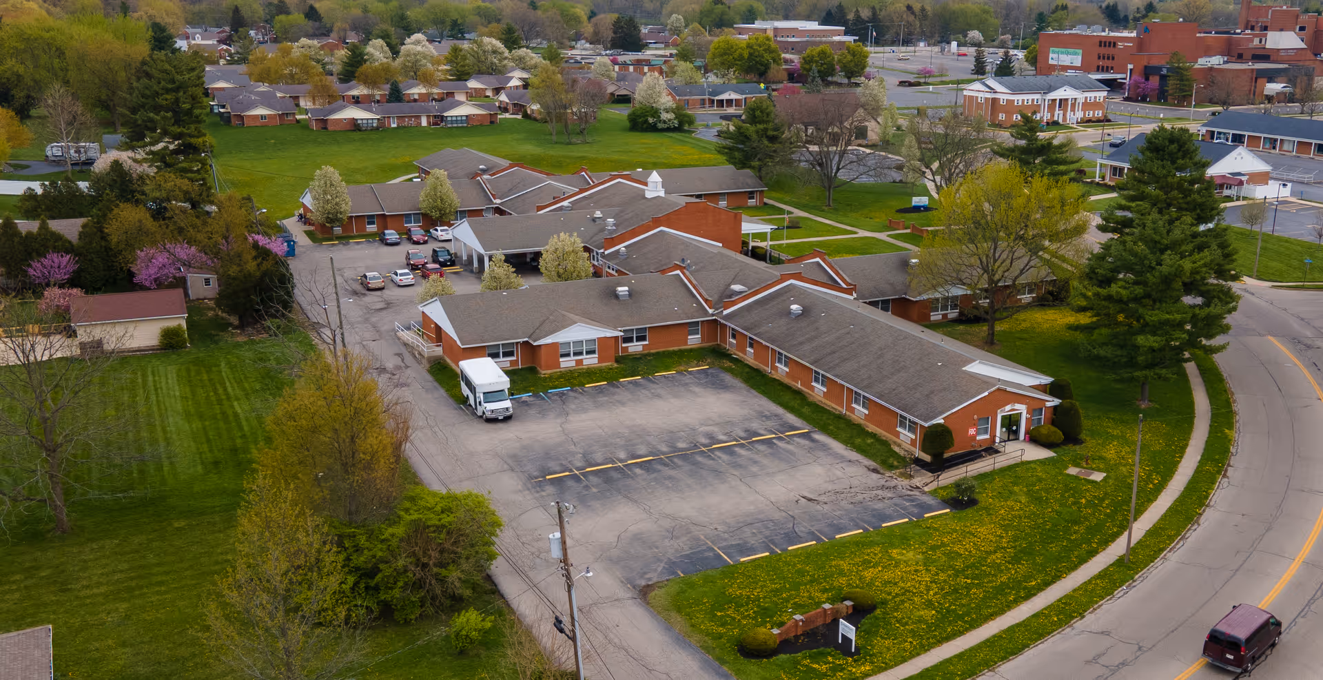 Aerial view of a brick senior living campus with parking and green lawns.