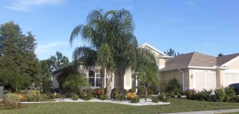 Front view of a single-story senior living facility with landscaped entry and palm trees.