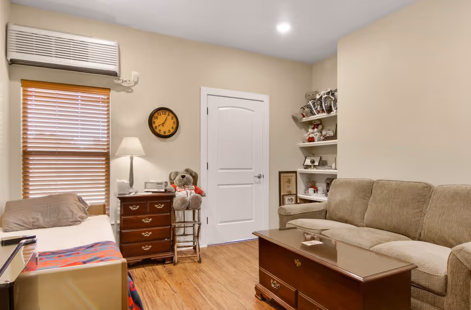 Cozy living room with beige sofa, coffee table, bed, shelves, and clock