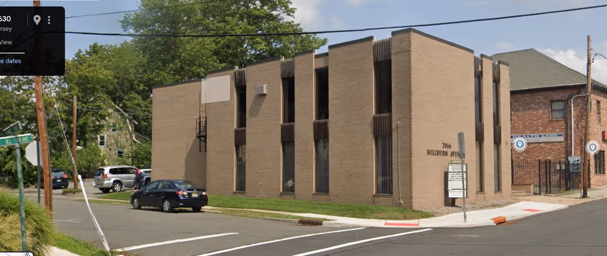 Exterior view of a tan brick senior care facility with parked cars and trees
