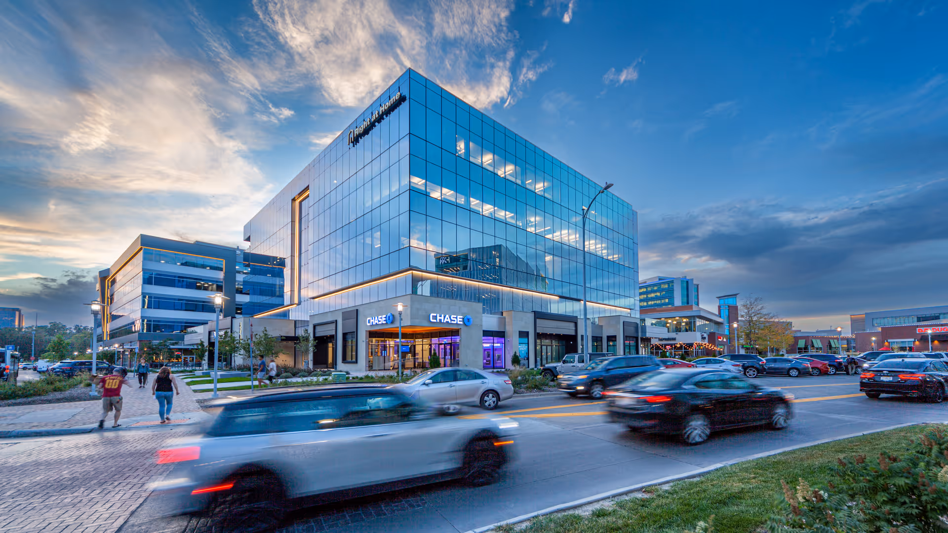 Modern glass corporate building facade with traffic and pedestrians on a city street.
