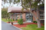 The brick facility entrance features a striped awning, glass doors, trees, and landscaped walkway.
