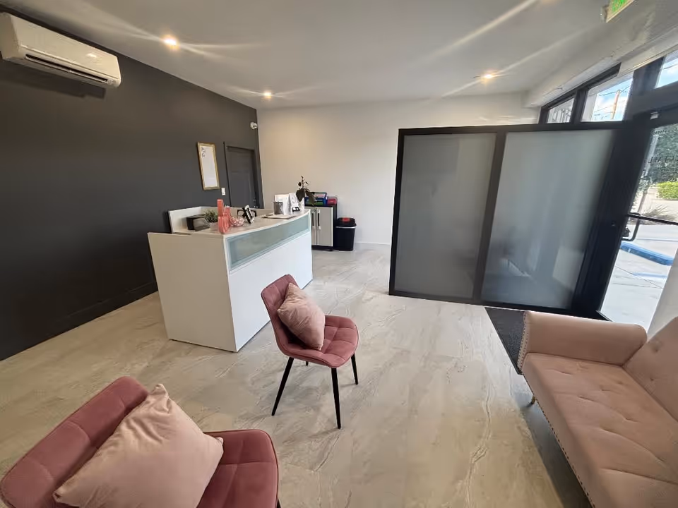 Modern lobby with white reception desk, pink lounge chairs, sofa and glass partition.
