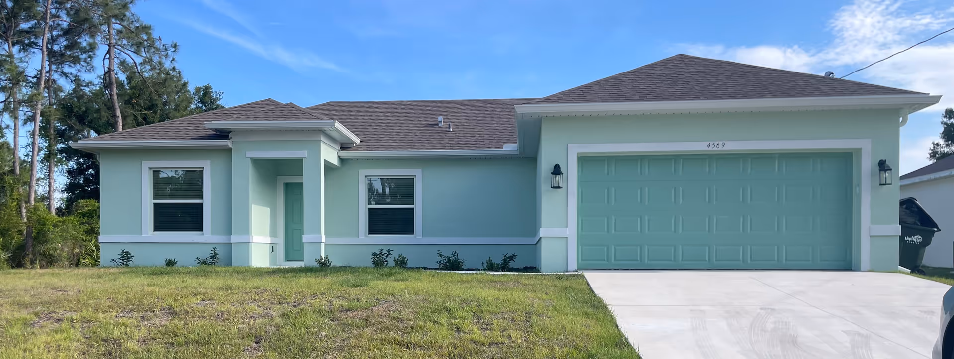 Single-story mint-green senior living facility front, with two-car garage, driveway, and landscaped lawn.