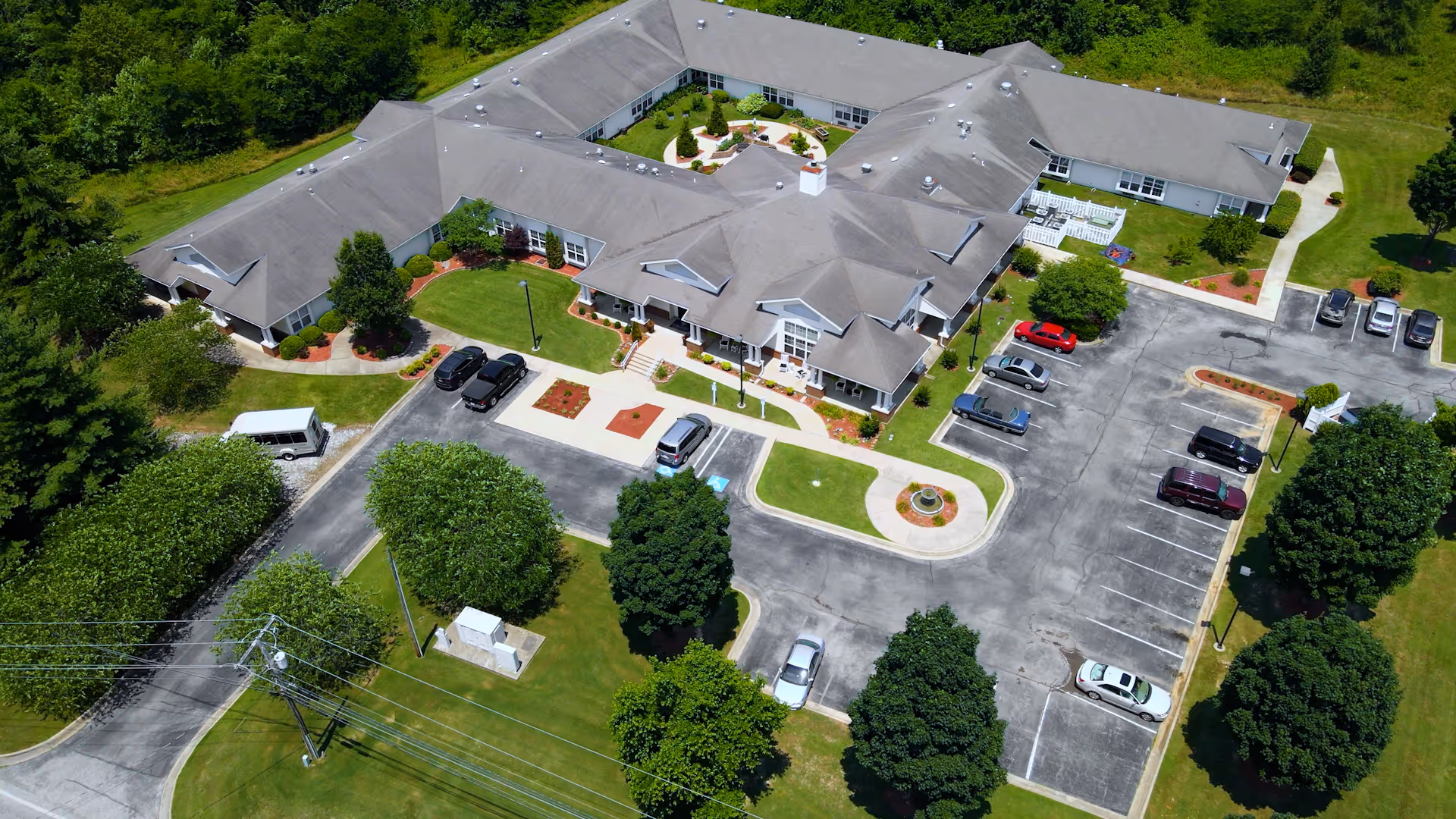 Aerial view of a U-shaped senior living building with a central courtyard, parking lot, driveways, and surrounding trees.
