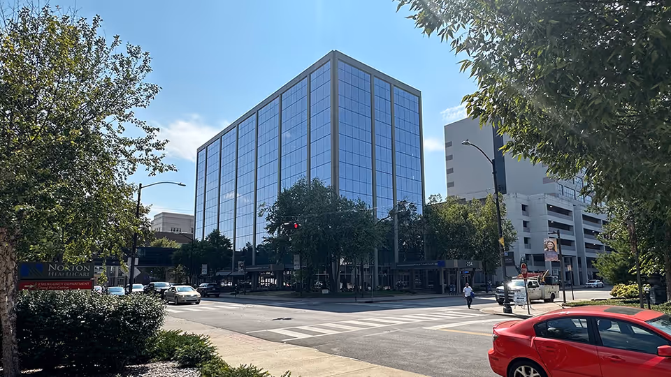 Tall glass-front medical tower on a city street with trees and crosswalk nearby.