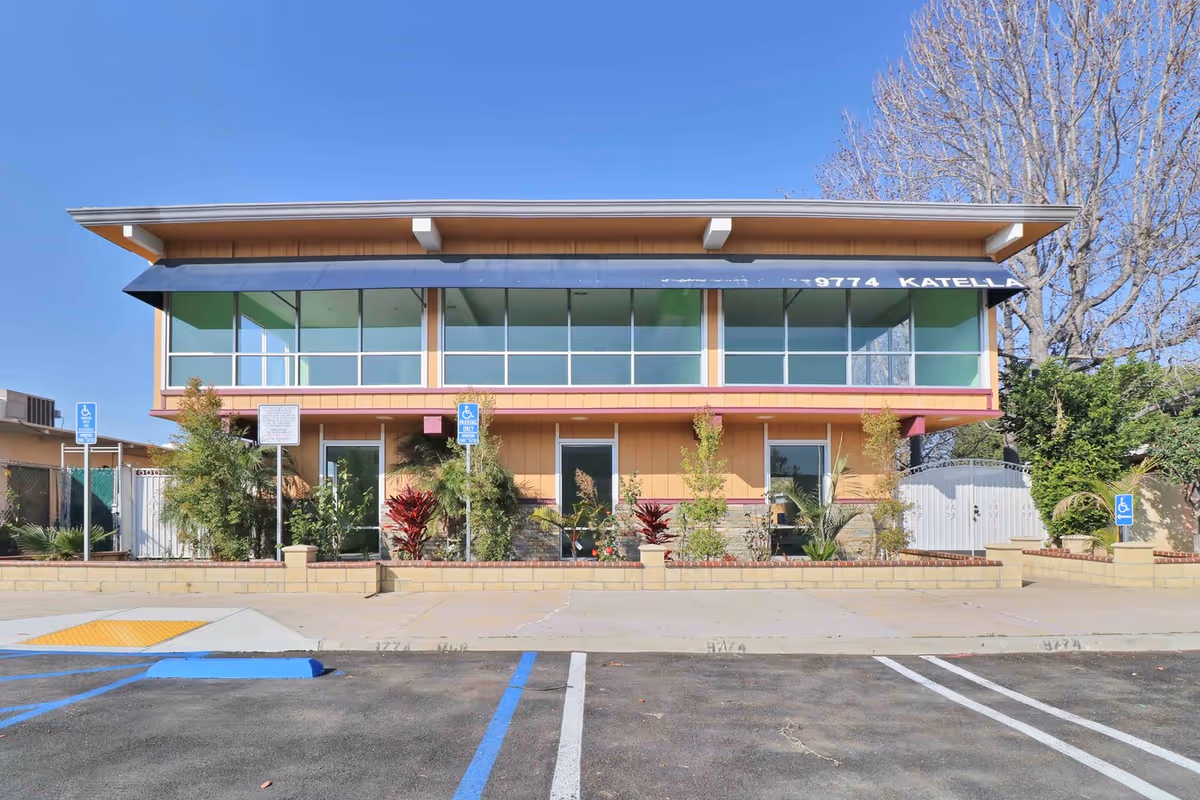 Two-story modern senior facility with large windows and a parking lot in front.
