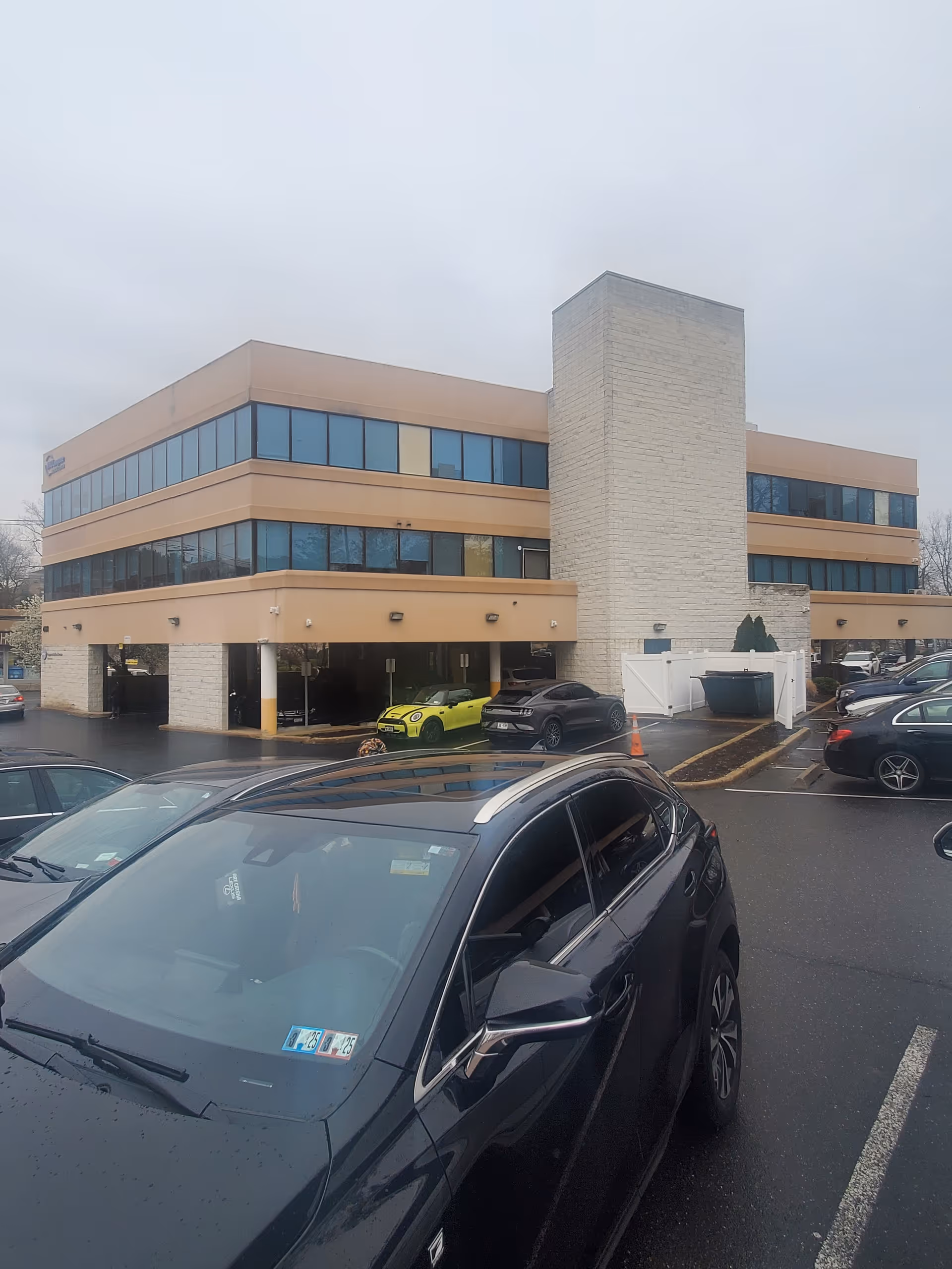 Exterior view of a beige, two-story medical building with large windows and parked cars.