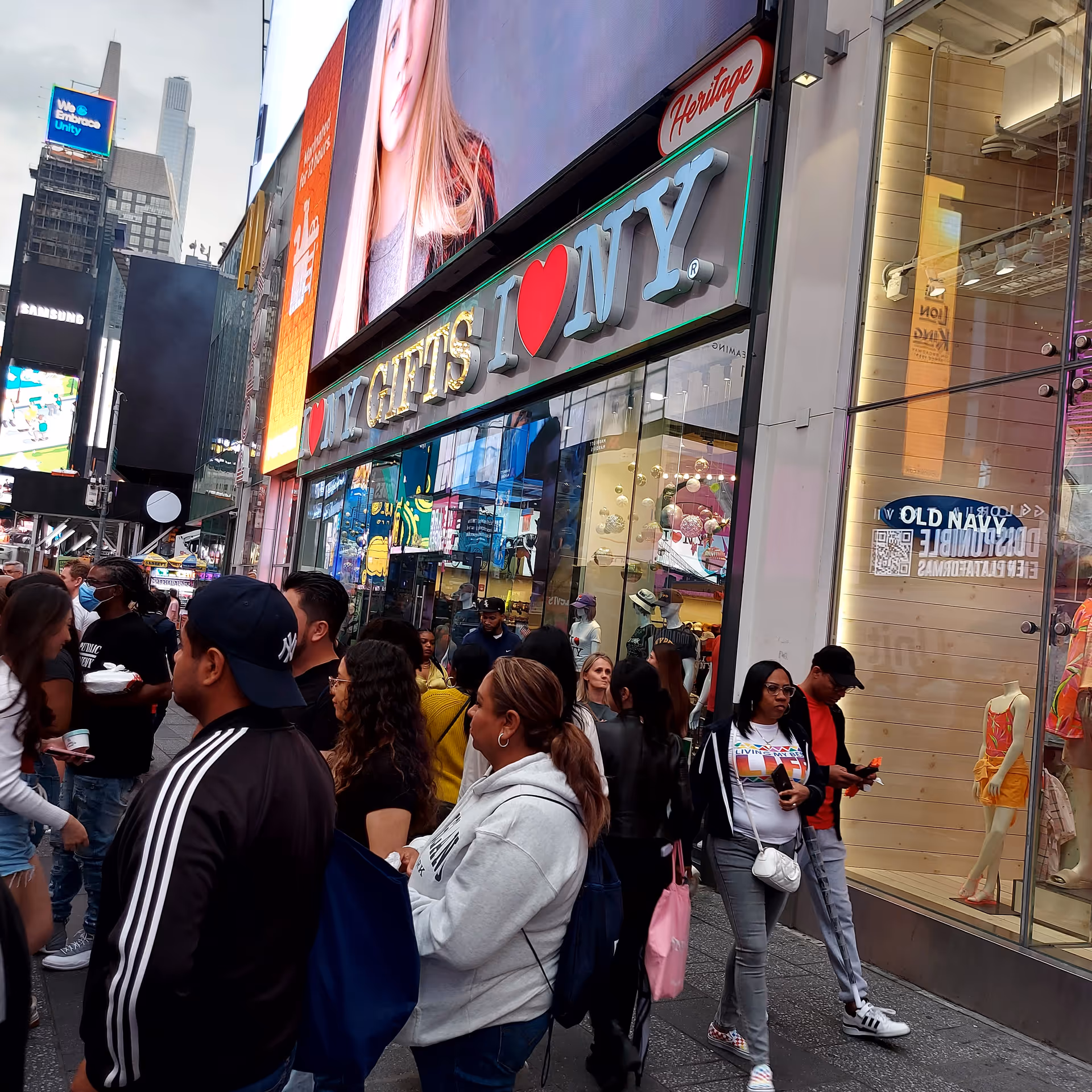 Busy city street with shoppers outside a bright storefront displaying I Love NYC.