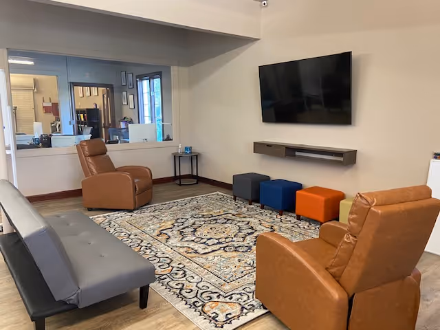 A lounge area with brown leather recliners, a sofa, colorful ottomans, and a wall-mounted TV.
