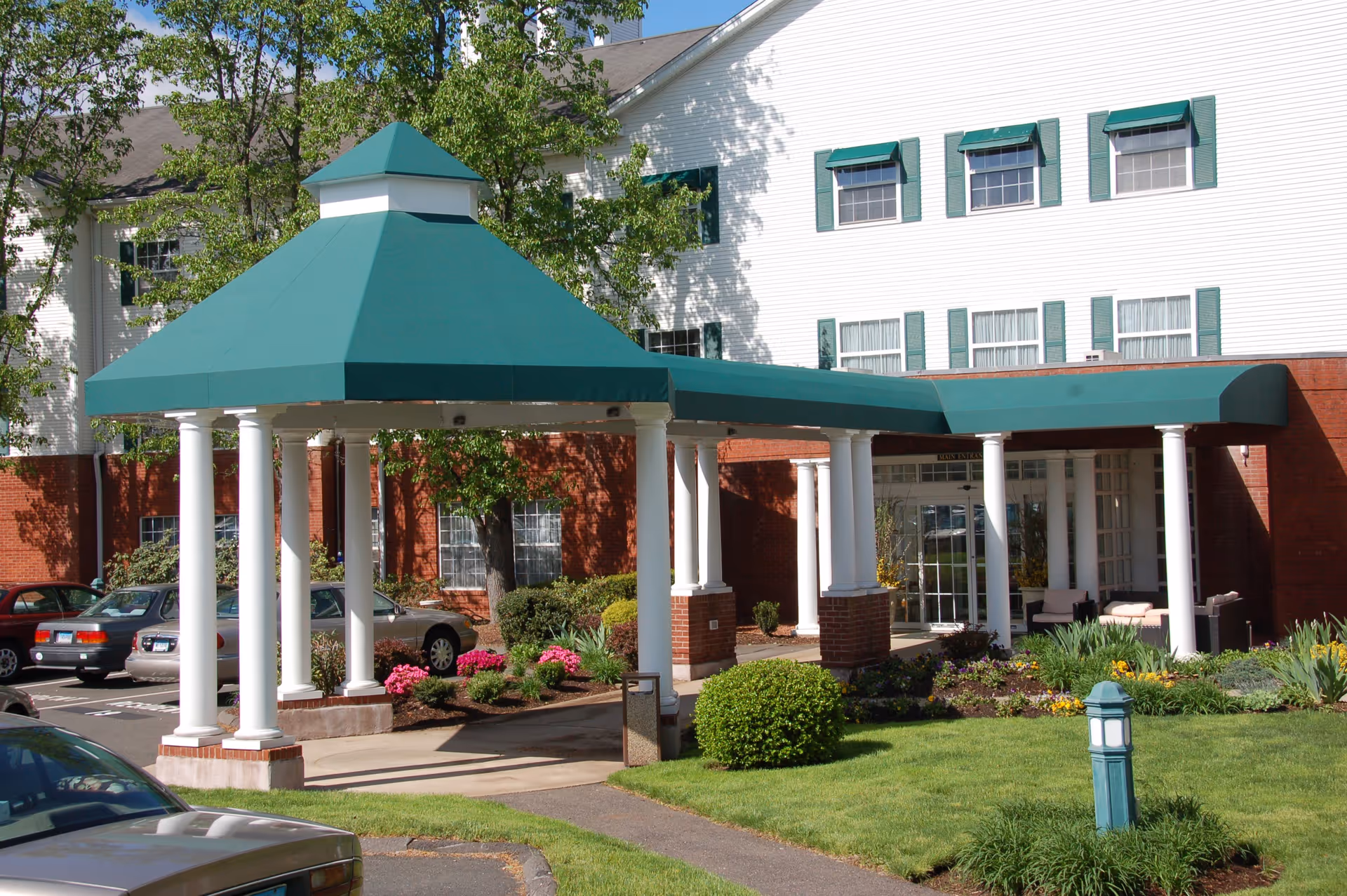 Front view of a senior living facility entrance with green canopy and plants.