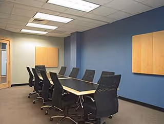Conference room with a long table, black rolling chairs, blue walls, and wall-mounted cabinets.
