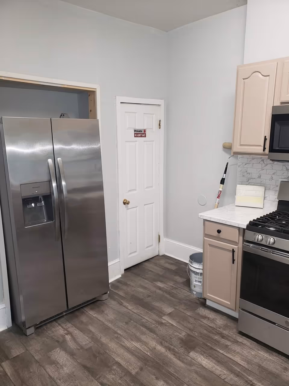 Modern kitchen with stainless steel refrigerator and stove, beige cabinets, and a white doorway.