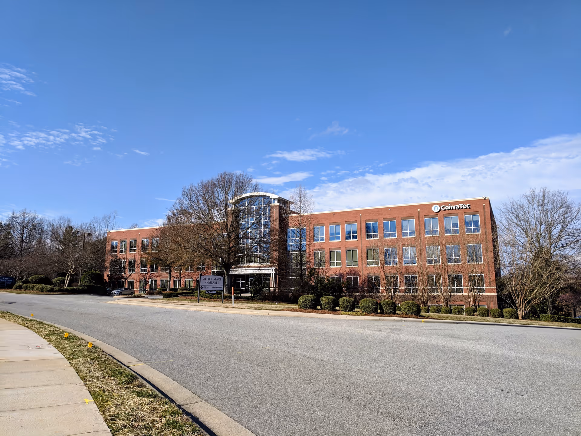 Brick building with a glass atrium entrance along a curved road under a blue sky.