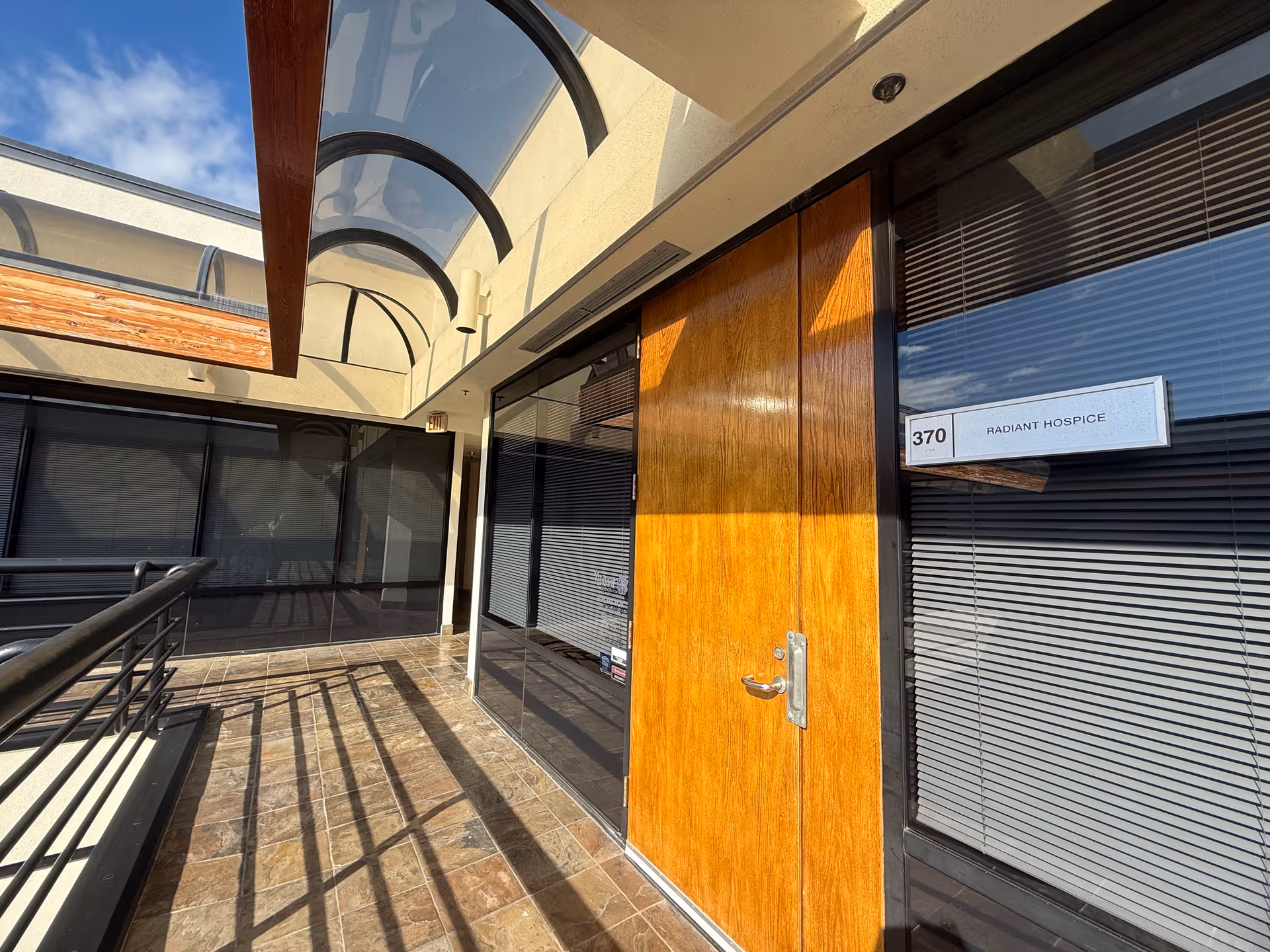 Exterior view of a facility entrance with glass doors, a wooden door, and curved glass canopy.