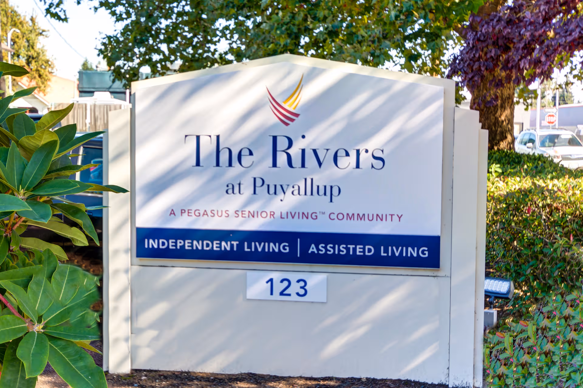 Outdoor sign for The Rivers at Puyallup senior living community beside greenery.