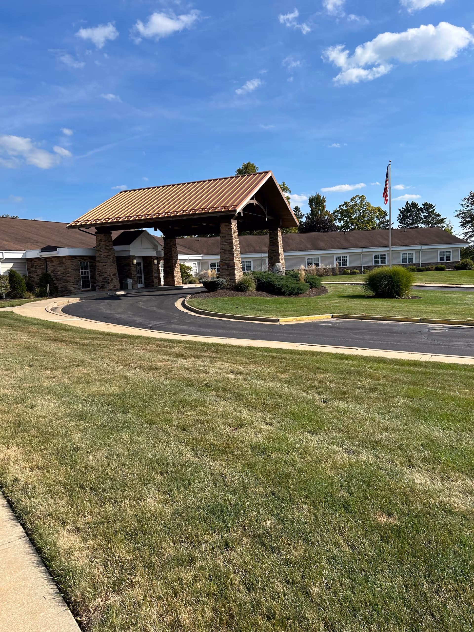 Exterior view of WellSpring Hospice facility with covered entrance, driveway, lawn, and flag.