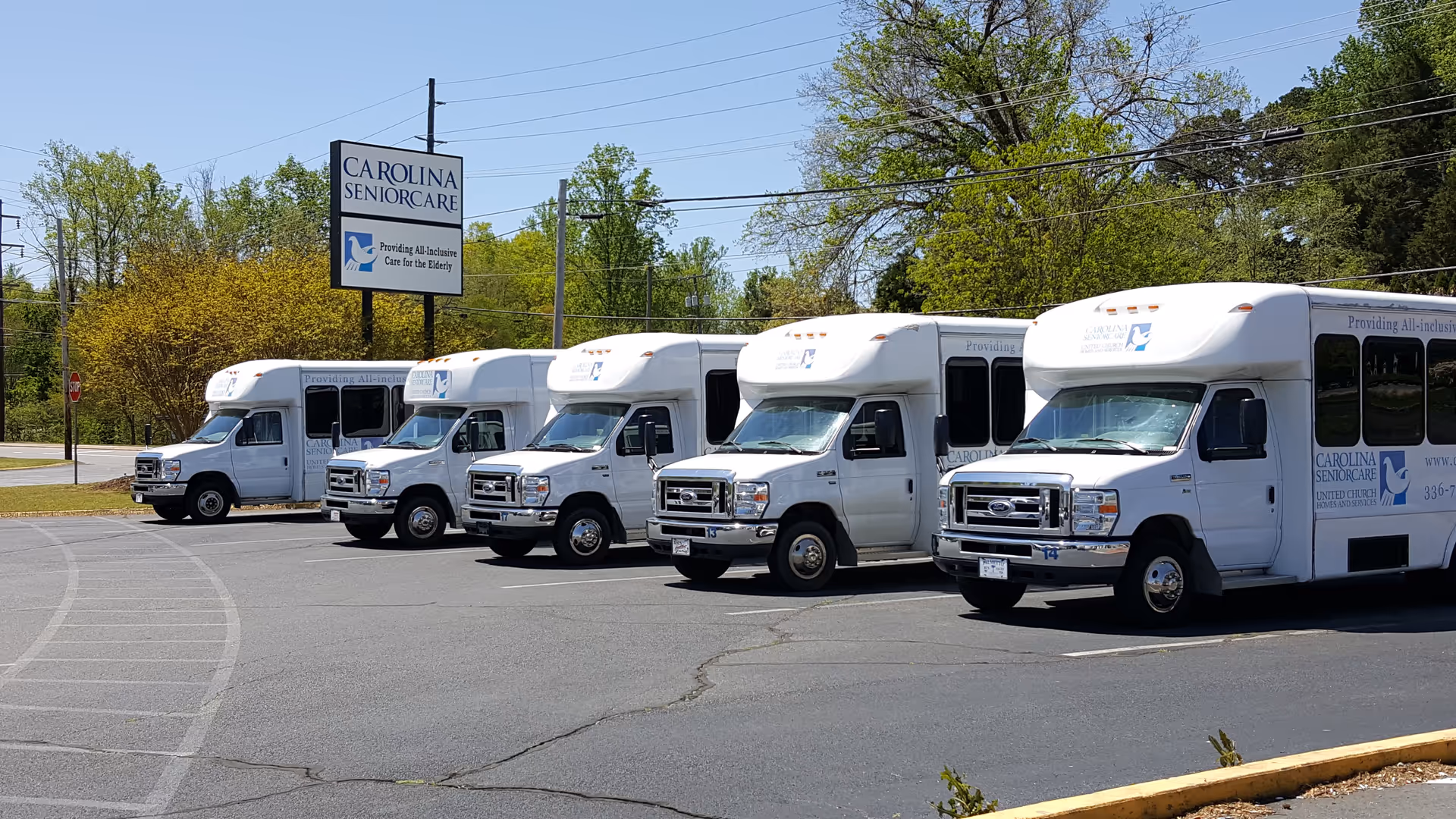 Line of white shuttle buses parked in front of the Carolina SeniorCare facility.