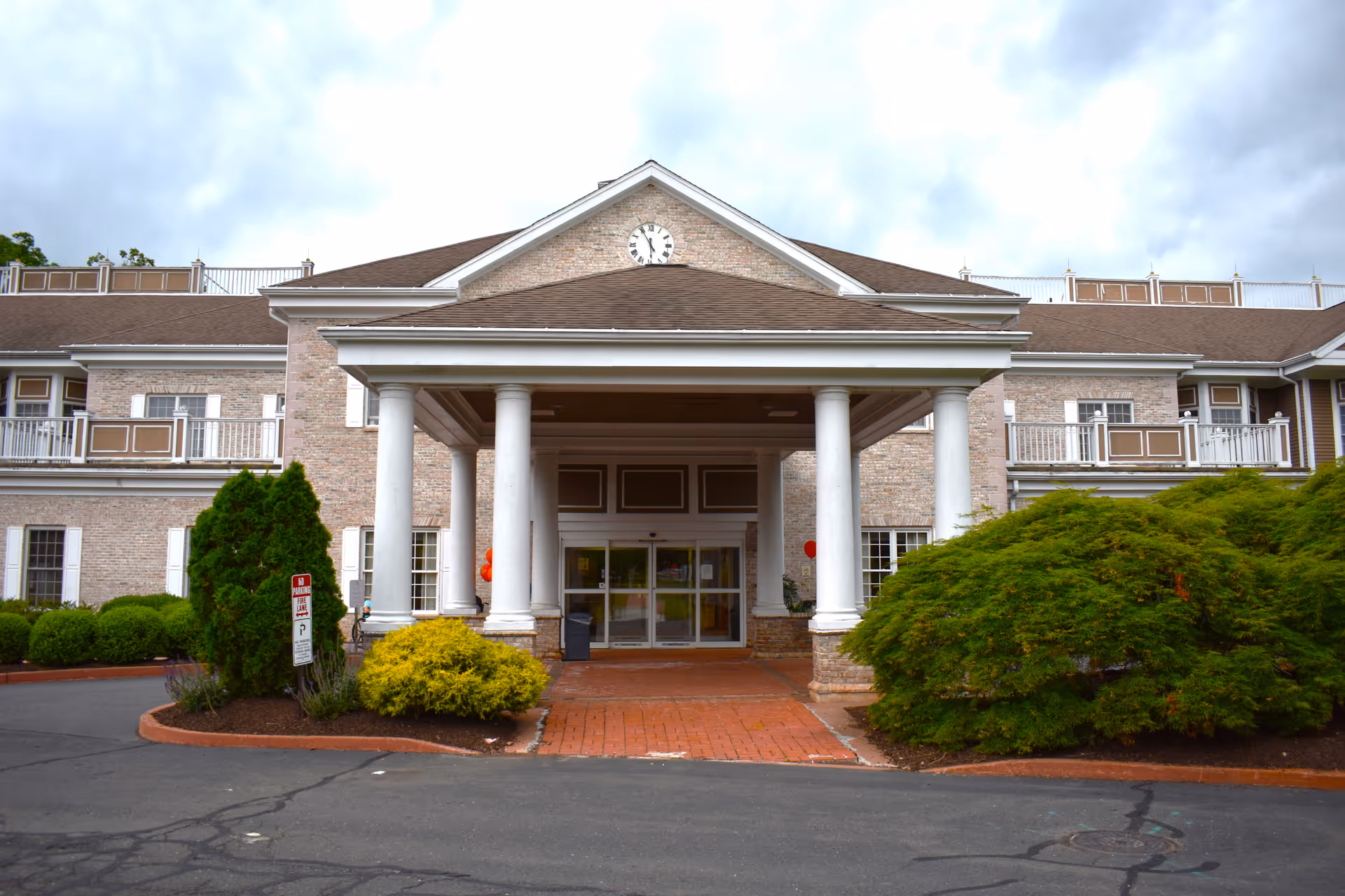 Front entrance of a brick senior living building with white columns, a covered portico, and landscaping.