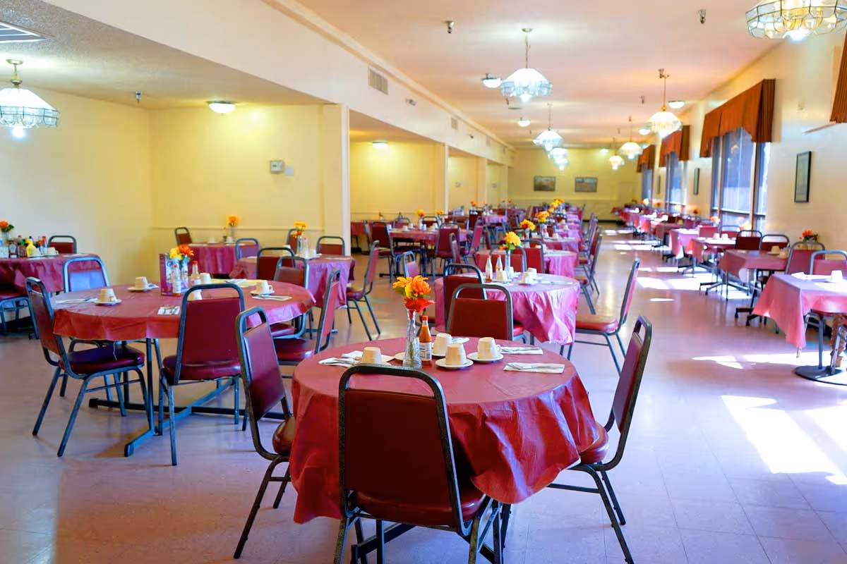 Large dining hall with round tables covered in red tablecloths, chairs, place settings, and floral centerpieces.