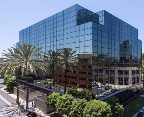 Glass-front modern building with palm trees and a parking lot.