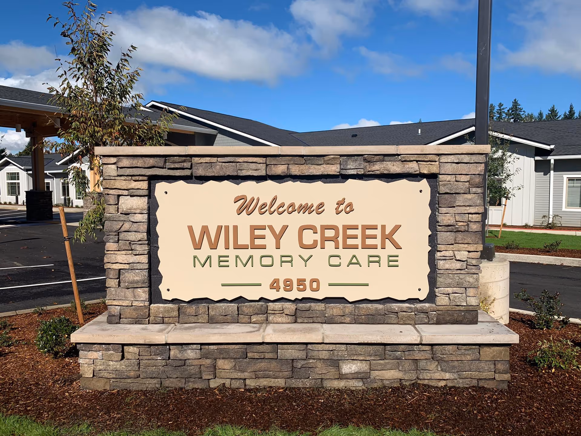 Stone entrance sign reads 'Welcome to Wiley Creek Memory Care' with the building exterior
